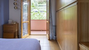 Une chambre à coucher avec un lit, une commode en bois, une fenêtre avec des rideaux et une vue sur l’extérieur.