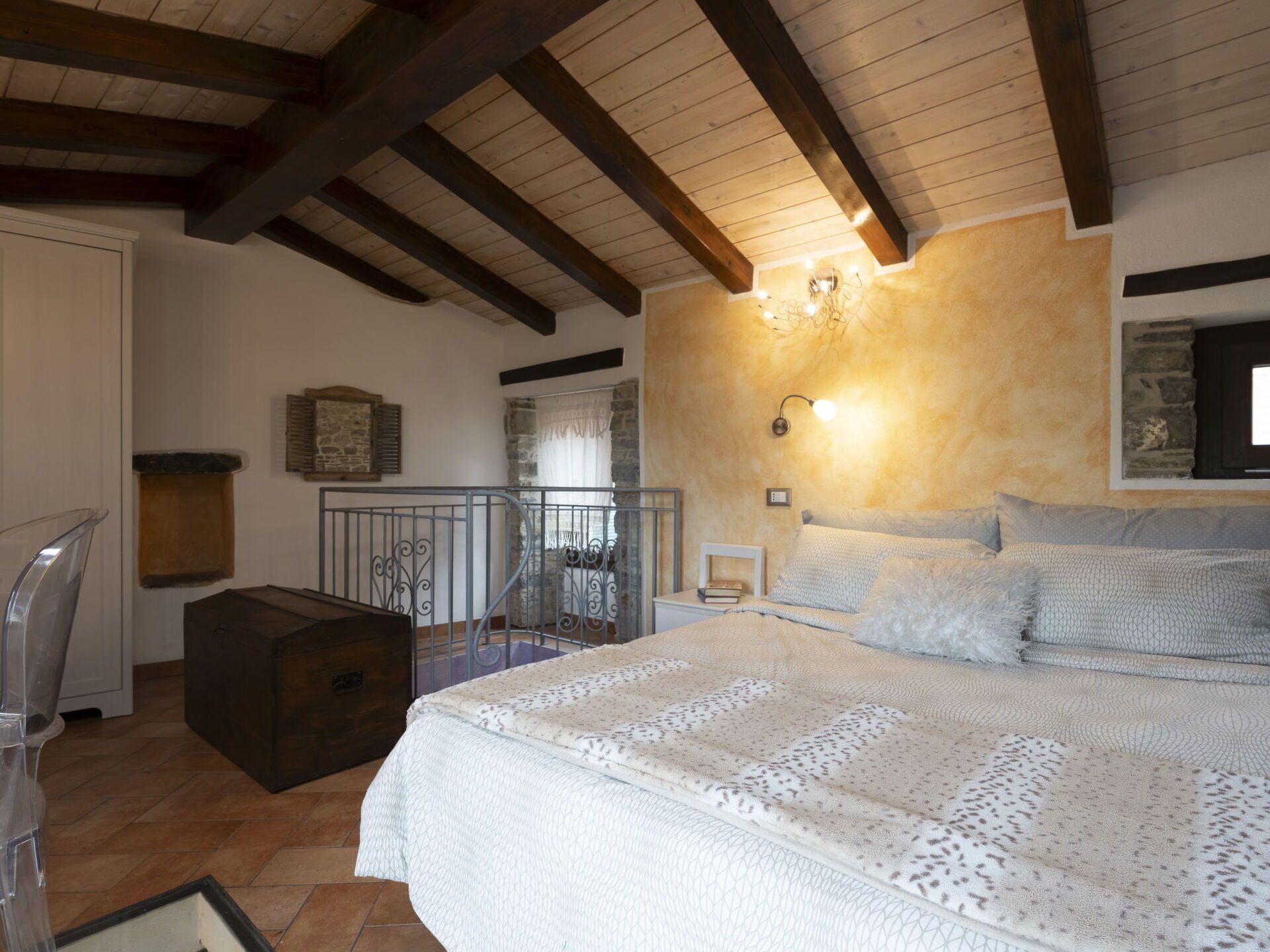 A bedroom with a large bed, wooden beams, a stone wall, and a small balcony.