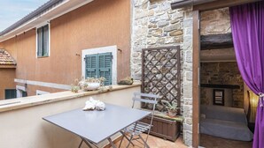 Un patio con una mesa y sillas, un muro de piedra y una ventana con contraventanas.