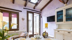 Comedor con mesa preparada para cuatro personas, un televisor sobre el mueble bajo y una ventana con vistas al exterior.