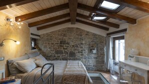 Un dormitorio con pared de piedra, una cama con cabecera, una mesita de noche, una silla y una ventana con vistas.