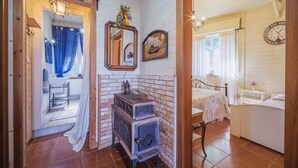 Une chambre rustique avec une cheminée en briques, un lit à baldaquin et une salle de bain équipée d’un lavabo et d’un miroir.