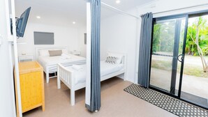 Une chambre d’hôtel moderne équipée d’un lit, d’un bureau, d’une télévision et d’une porte-fenêtre coulissante donnant sur un jardin.