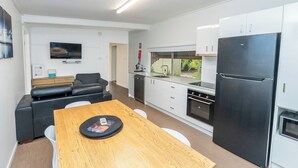 Une cuisine compacte avec des meubles blancs, un réfrigérateur noir et un coin repas comprenant une table et des chaises en bois.