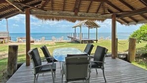 Un espace extérieur abrité, avec une table et des chaises, offrant une vue sur une plage et l’océan.