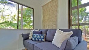 Ein Zimmer mit grauem Sofa, einem Fenster mit Blick auf Grünflächen und Holzboden.