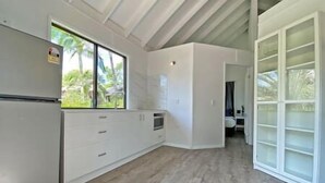 Una cocina con horno integrado, ventana con vista a follaje, y un armario blanco.