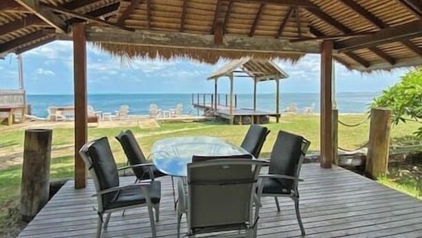 Un espacio de estar al aire libre con techo, con una mesa y sillas, con vistas a la playa y al océano.