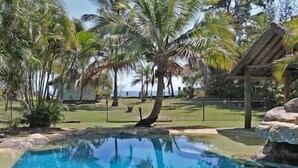 Zona de piscina con palmeras y vista al océano.