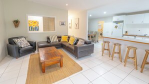 Una sala de estar moderna con un sofá modular, una mesa de centro y una zona de cocina con taburetes de bar.
