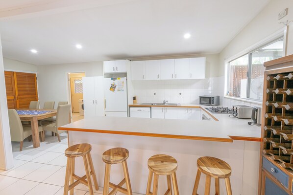A modern kitchen with white cabinets, a central island with stools, a dining area with a wooden table, and a wine rack.