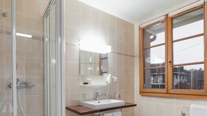 Ein Badezimmer mit einer Duschkabine, einem Waschbecken mit Spiegel darüber und einem Fenster mit Holzrahmen.
