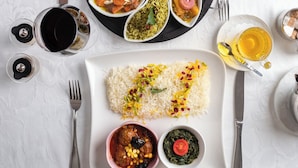 Ein Tisch ist reichhaltig mit Speisen gedeckt, darunter Reis, Salat und mehrere Curry-Schüsseln, dazu Gläser Tee und Wasser.