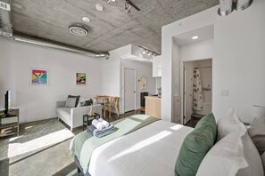 Una habitación de hotel moderna con cama, sofá, escritorio y zona de ducha.