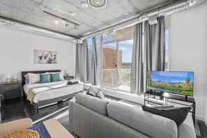 Una habitación de hotel moderna con una cama grande, un sofá, un televisor y un balcón con vistas a la ciudad.