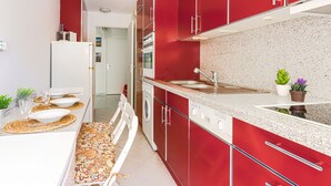 Une cuisine moderne avec des meubles rouges, un évier en acier inoxydable et un coin repas avec une table dressée pour quatre personnes.