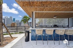 An outdoor bar with a wooden ceiling, a city view, and three wicker bar stools. - 37th Floor Studio - Balcony with Bay Views & Pool (Miami)