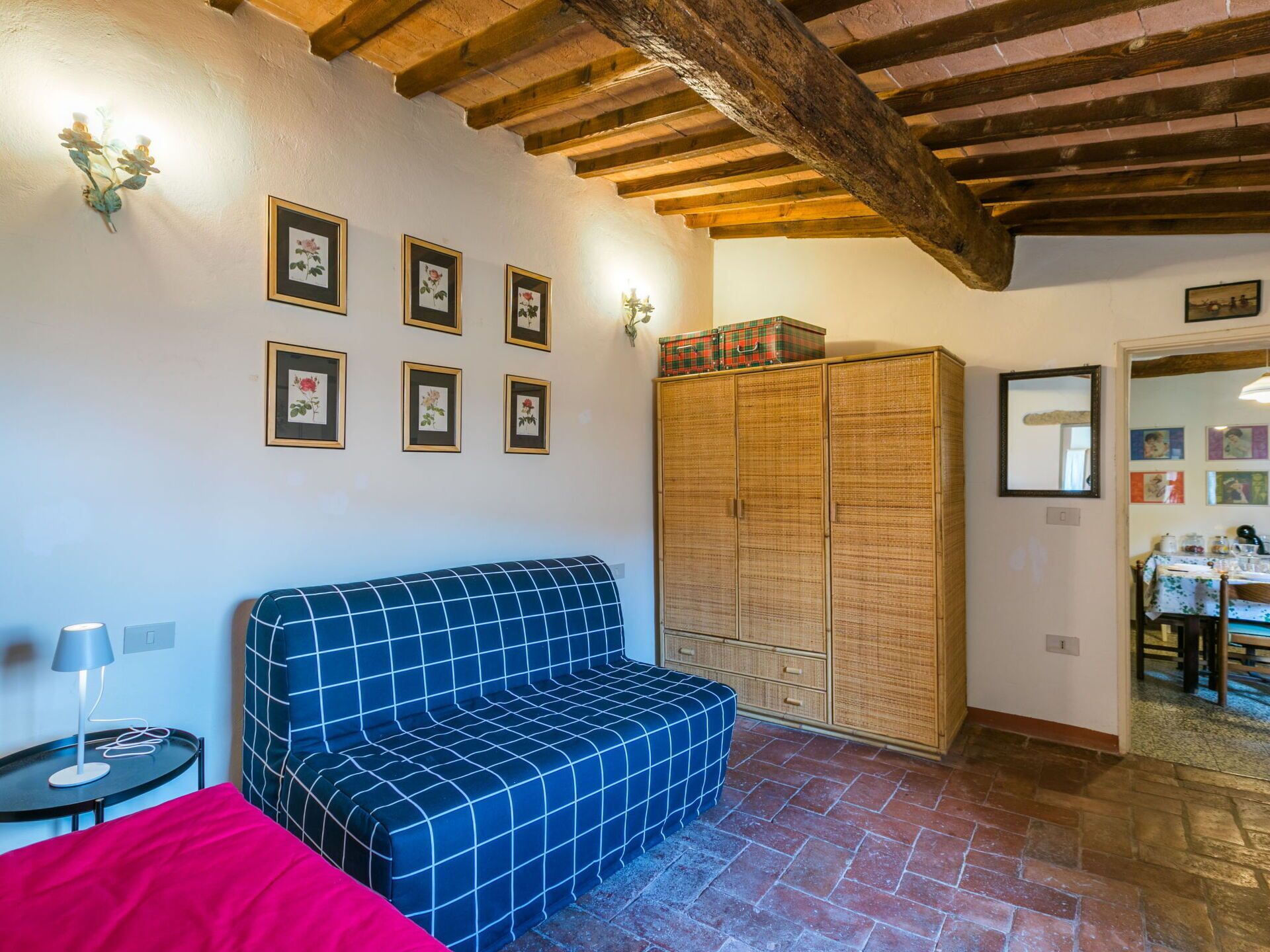 Una habitación con un sofá azul a cuadros, un armario de madera y cuadros con motivos florales en la pared.