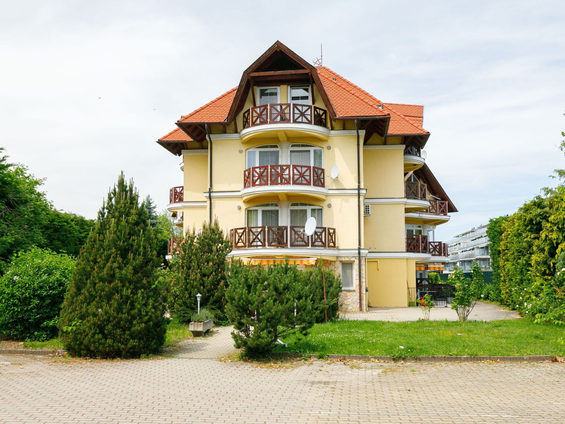 A multi-story building with balconies, a brick pathway, and surrounding greenery.