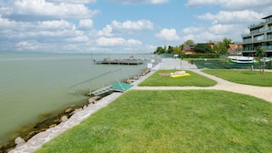A lakeside view with a dock, grassy areas, and buildings in the background. - Cosy apartment for 4 guests with A/C, WIFI, TV and terrace (Tapolca)