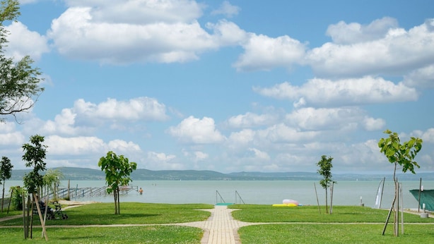 A paved pathway leading to a body of water with a clear sky and distant mountains. - Cosy apartment for 4 guests with A/C, WIFI, TV and terrace (Tapolca)