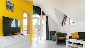 A modern living room with a flat-screen TV on a white cabinet, a grey sofa with yellow cushions, and a white coffee table.