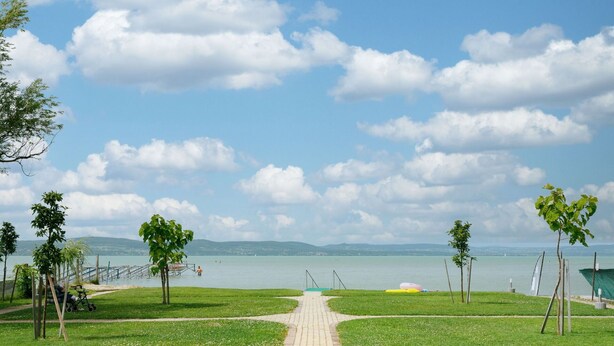 A paved pathway leading to a body of water with a clear sky and distant mountains.
