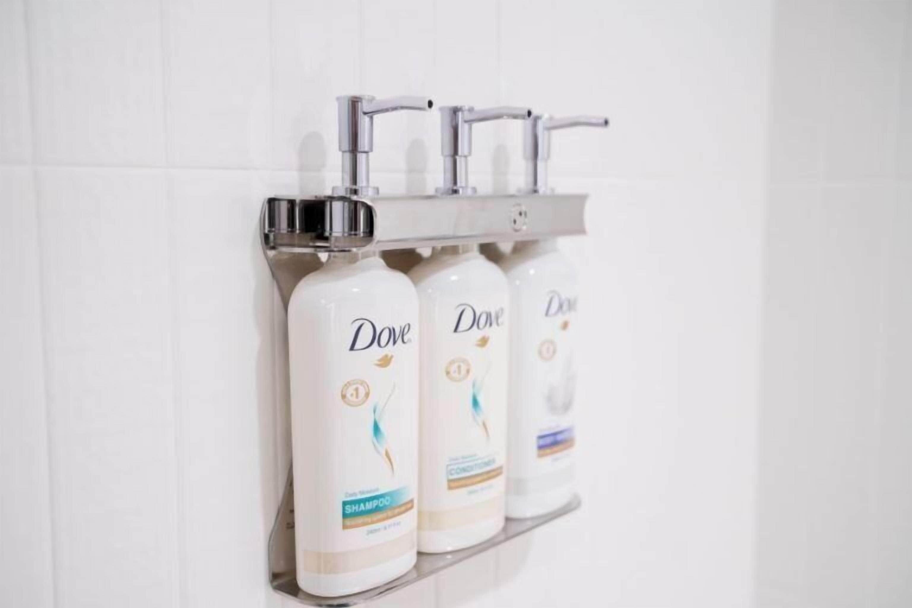 Three Dove shampoo bottles on a white tiled wall with a silver faucet above them.
