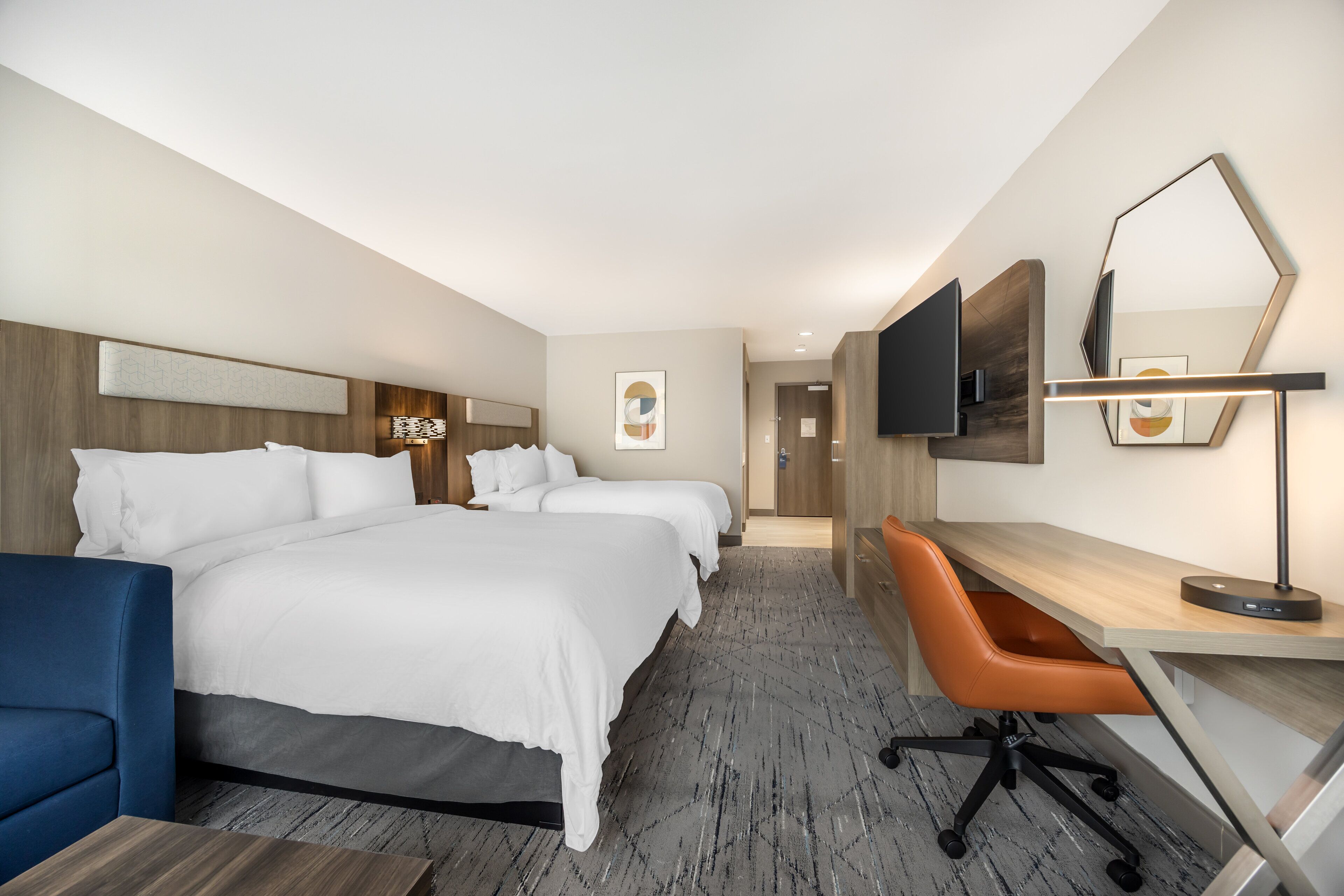 A hotel room with two beds, a desk, a chair, a TV, and a mirror.