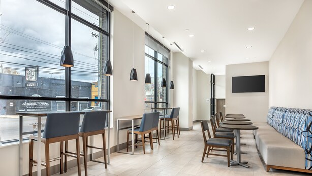 Un intérieur moderne avec de grandes fenêtres, un long banc et plusieurs tables et chaises.