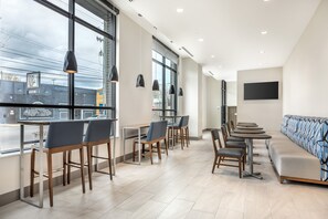 A modern interior with large windows, a long bench, and multiple tables and chairs.