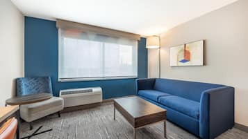 A modern living room with a blue sofa, a small round table, a coffee table, and a wall-mounted air conditioner.