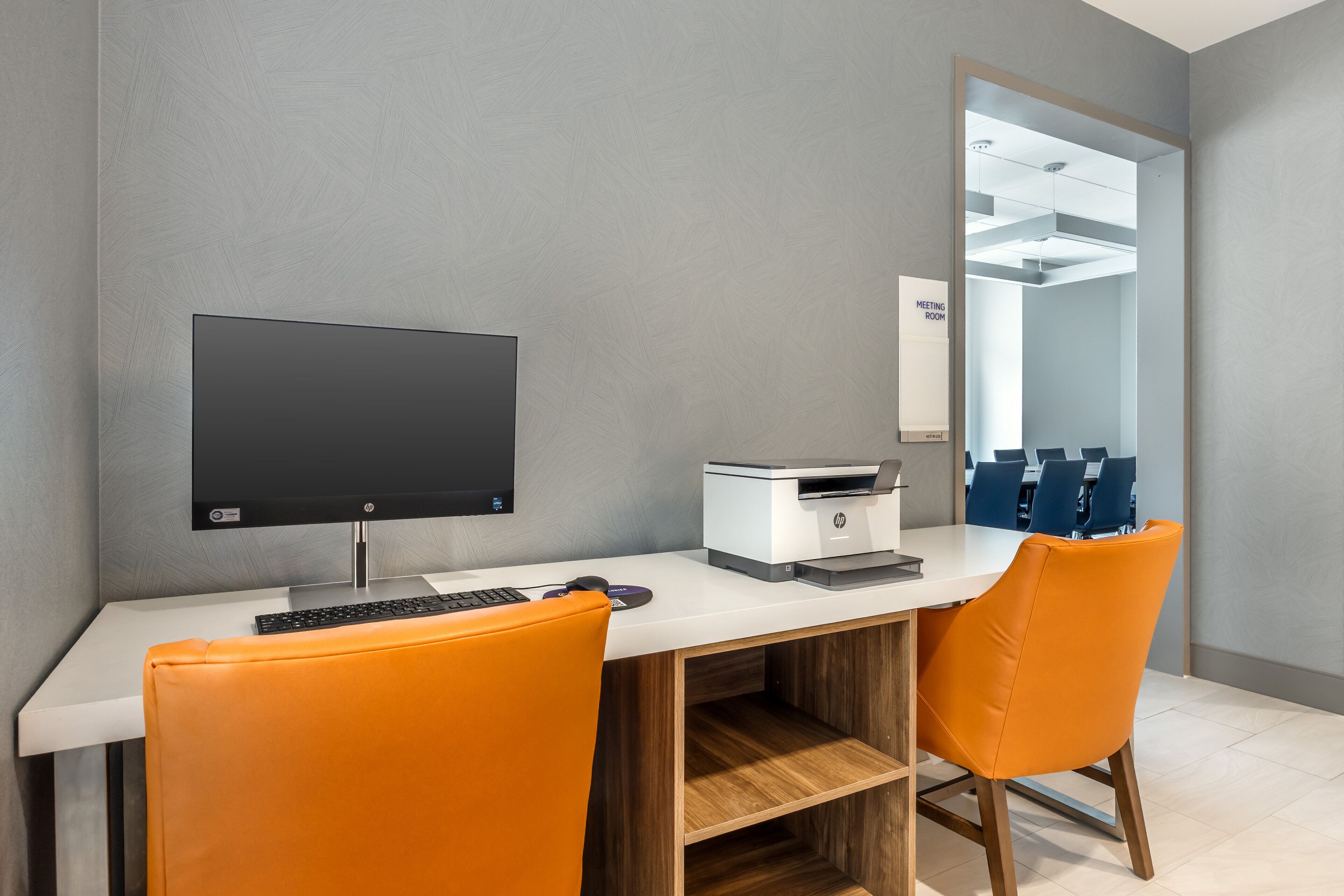 A modern office space with a desk, computer, printer, and two orange chairs.