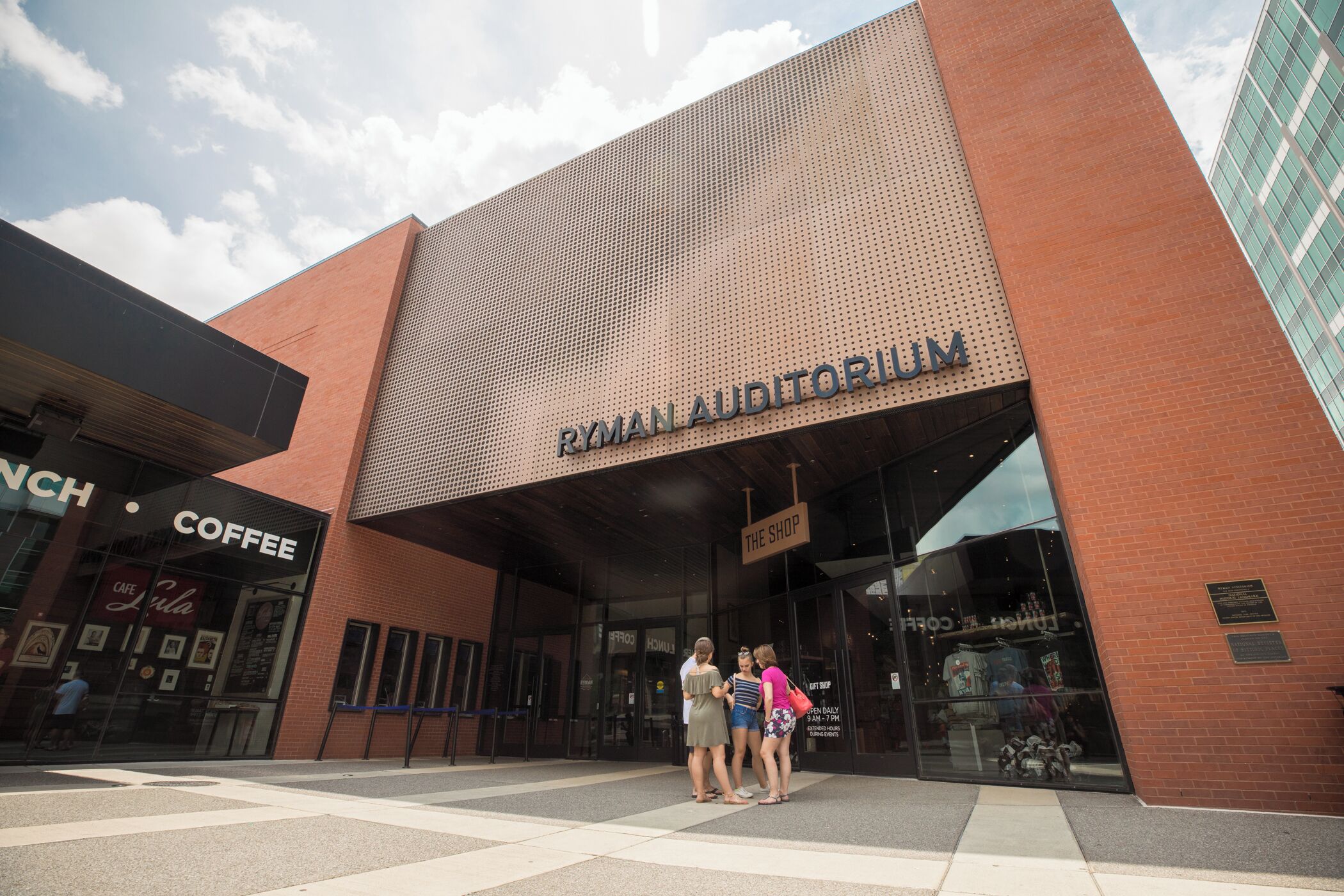 A building with a large sign reading "RYMAN AUDITORIUM" and a smaller sign for "THE SHOP".