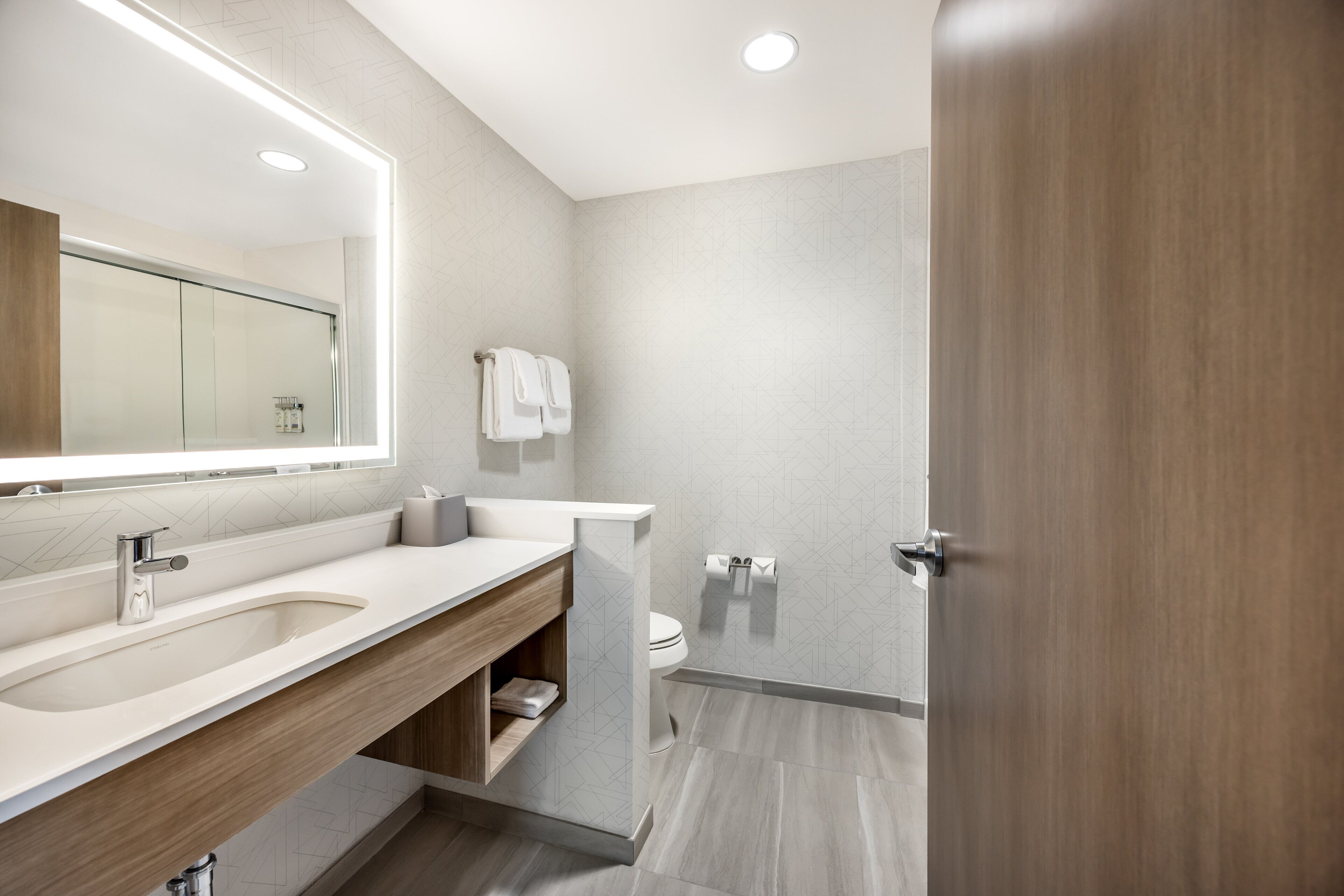 A modern bathroom with a large mirror, a sink, and a toilet.