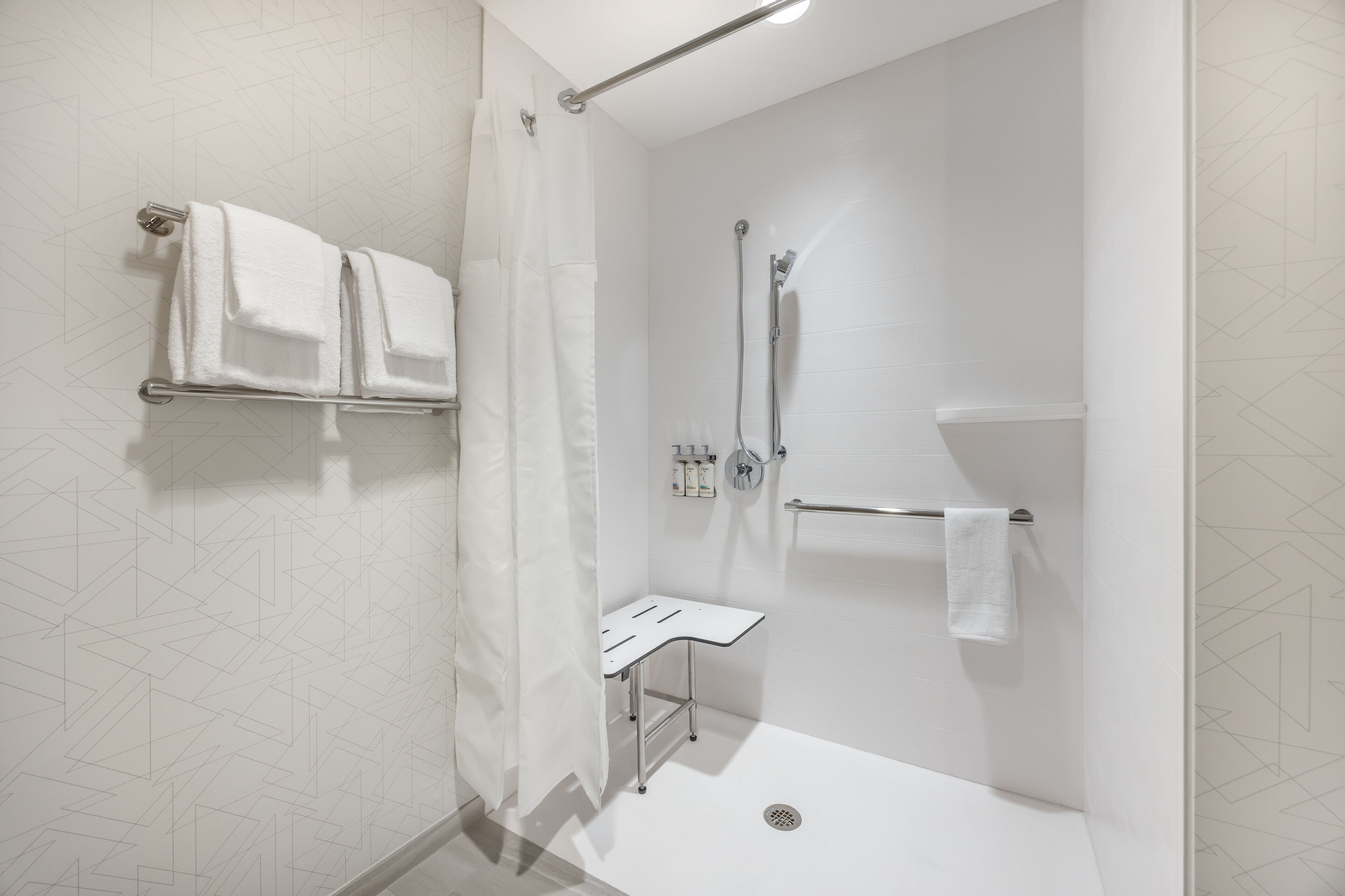 Ein modernes Duschbad mit Glastür, weißem Handtuchhalter, Duschbrause und einer kleinen, weißen Ablagefläche.