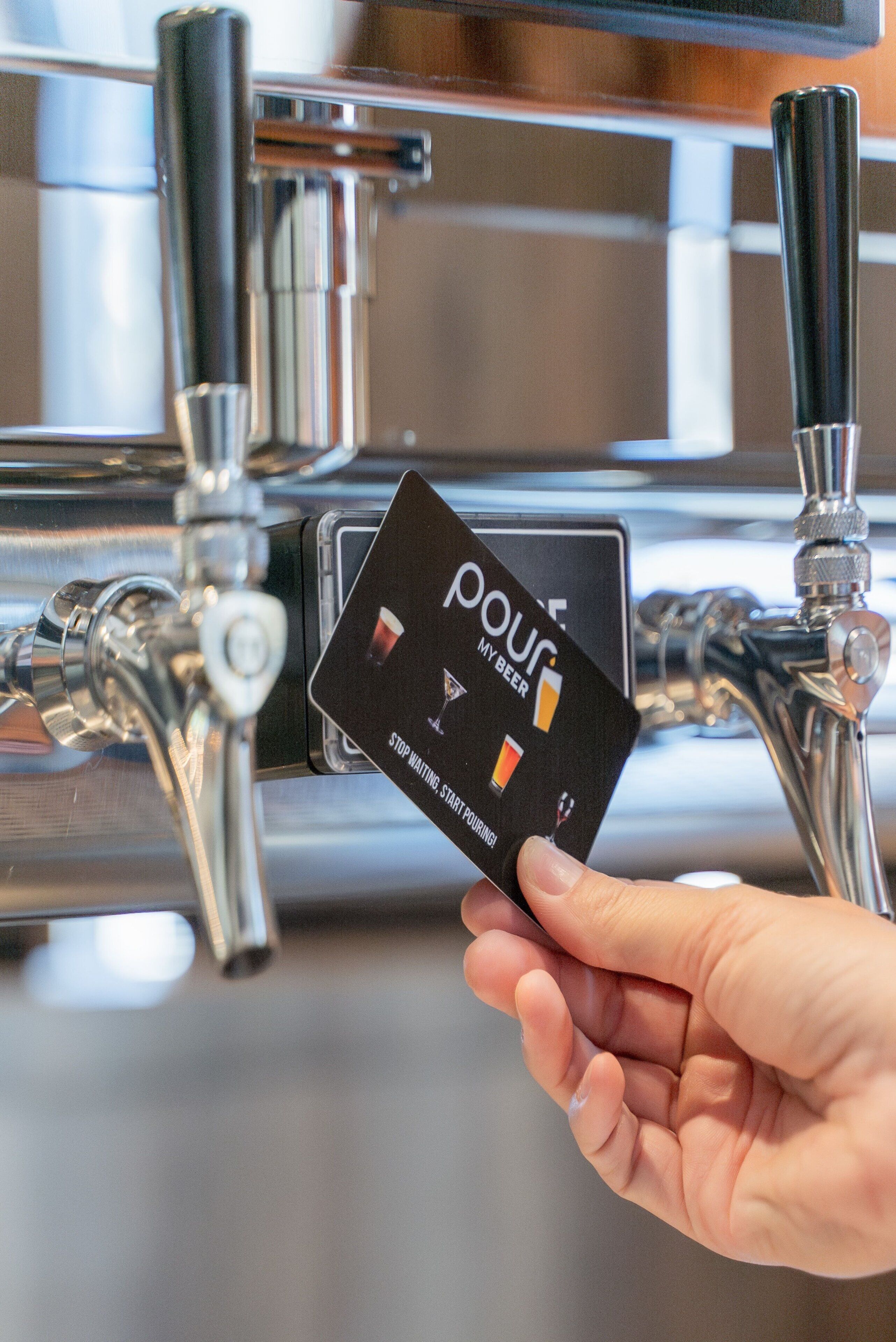 A hand holding a card with the text "pour my beer" and "stop waiting start pouring" in front of a beer tap.