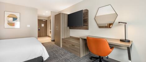 A hotel room with a bed, a desk, an orange office chair, a flat-screen TV, and a mirror.