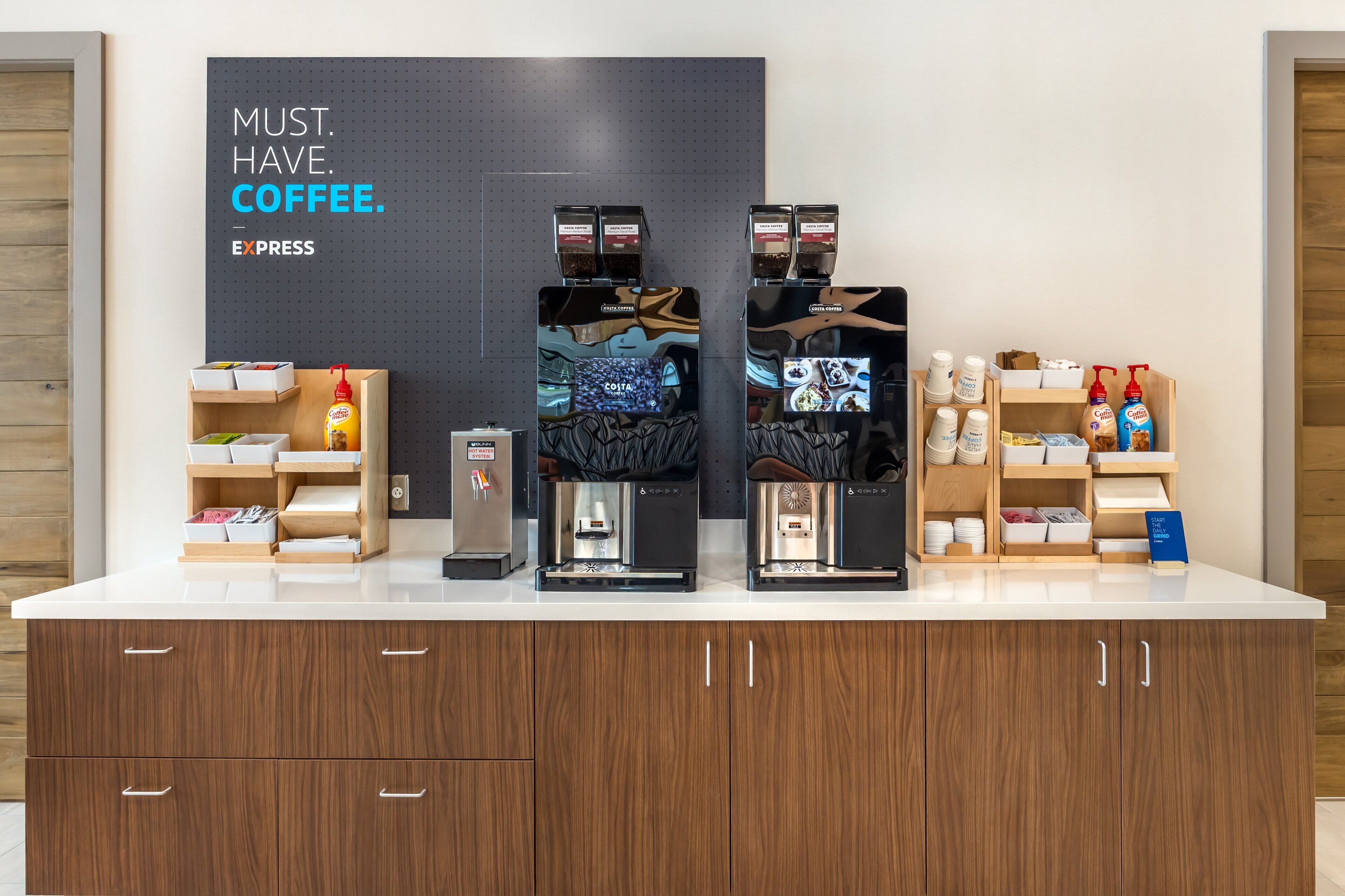 A coffee station with three coffee makers, a condiment dispenser, and a small refrigerator.