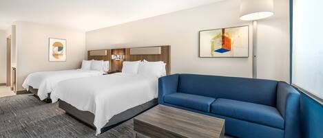 A hotel room with two beds, a blue sofa, a wooden coffee table, and artwork on the walls.