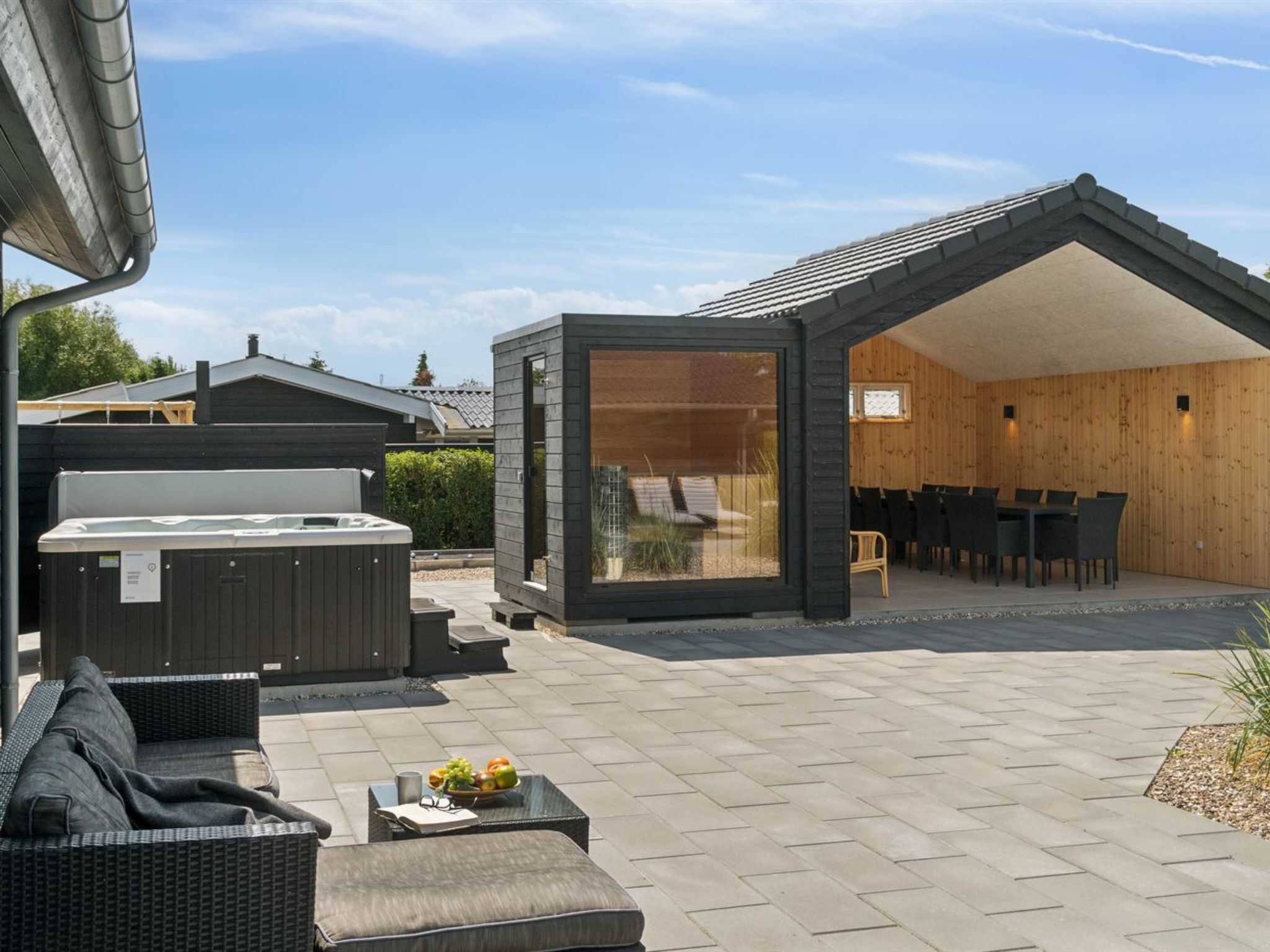 A modern outdoor patio with a hot tub, seating area, and a wooden dining space.