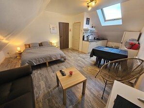 Une pièce compacte et bien éclairée, comprenant un lit, une petite table, une chaise et un coin cuisine.