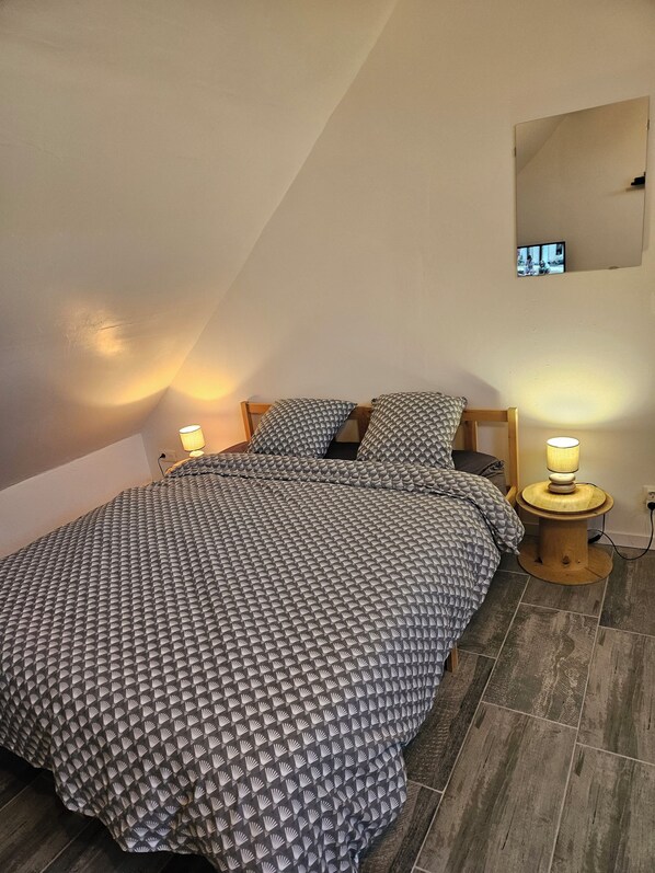 A bedroom with a bed, two bedside lamps, a small table, and a wall-mounted TV.