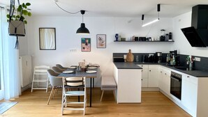 Una cocina moderna con armarios blancos, una zona de comedor con sillas y una planta colgante.
