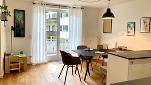 Una cocina moderna con comedor, suelo de madera y vistas a un balcón con vegetación.