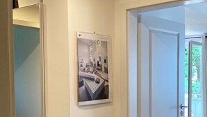 Un pasillo con una puerta blanca, un cuadro enmarcado en la pared y piso de madera.