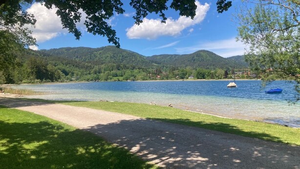 Vista de un lago con un camino despejado que lleva al agua, rodeado de exuberante vegetación y colinas al fondo.