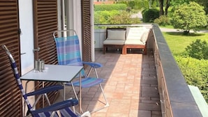 Un espacio de estar al aire libre cubierto, con mesa y sillas, que da a un jardín ajardinado y colinas lejanas.