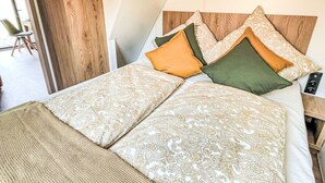 A bed with patterned bedding and pillows, a wooden headboard, and a view of an outdoor area with chairs. - Beautiful apartment in villa for 5 guests with A/C, TV, terrace and pets allowed (Fischbachau)