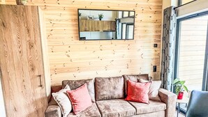 A cozy living room with a wooden wall, a large mirror, a brown sofa with red cushions, and a black chair. - Beautiful apartment in villa for 5 guests with A/C, TV, terrace and pets allowed (Fischbachau)